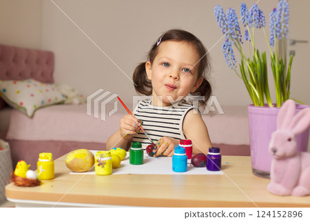 Little child girl paint Easter eggs at home. kid is preparing for Easter. 124152896