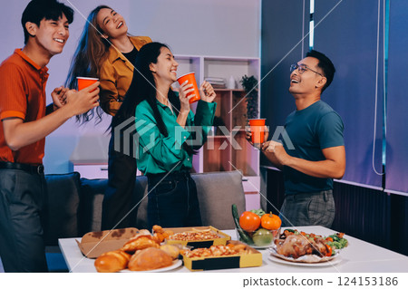 Happy young friends group having lunch at home. Asia family party eating pizza food and laughing enjoying meal while sitting at dining table together at house. Celebration holiday and togetherness. 124153186
