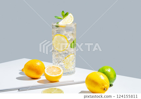 Lemonade with lemon, mint and ice in a glass on a white gray background with shadow and fruits. Lemonade with lemon, mint and ice in a glass on a white gray background with shadow and fruits. 124155811