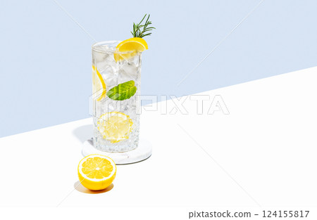Lemonade with lemon, rosemary and ice in a glass on a white  blue background. Summer citrus drink 124155817