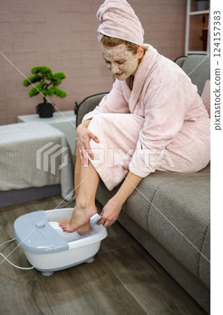 Woman enjoying a home spa day using a foot bath and face mask Woman enjoying a home spa day using a foot bath and face mask 124157383