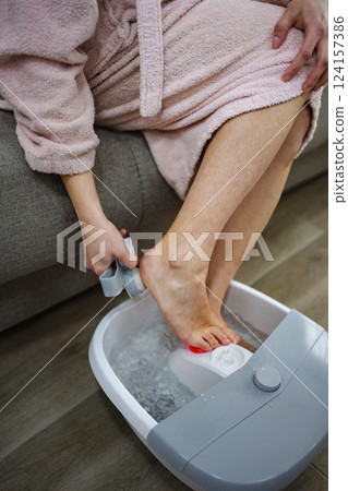 Woman enjoying a relaxing feet bath at home, using a pumice stone 124157386