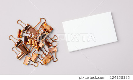 Heap of copper gold binder clips and memo note paper on light grey background 124158355