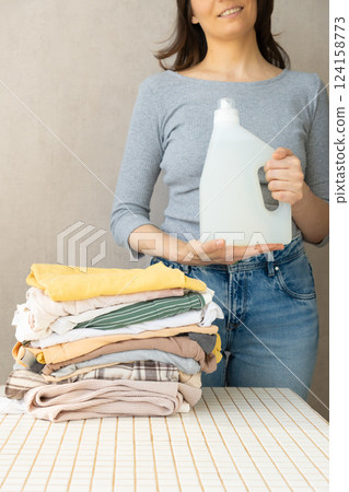 mockup, a happy woman holds a stack of clothes and a laundry gel or conditioner for washing clothes.  124158773