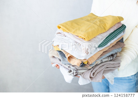 Laundry, woman holds stack of clothes in her hands after dry cleaning. housework, cleaning ironing. Laundry, woman holds stack of clothes in her hands after dry cleaning. housework, cleaning ironing. 124158777