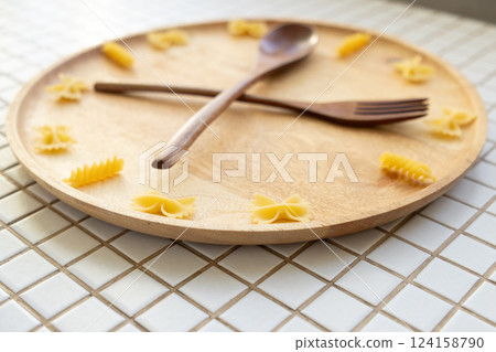 time to eat pasta. wooden plate with fork and spoon in form of clock hands. pasta on plate. time to eat pasta. wooden plate with fork and spoon in form of clock hands. pasta on plate. 124158790