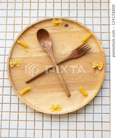 time to eat pasta. wooden plate with fork and spoon in form of clock hands. pasta on plate. 124158800