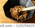 在木桌背景上，用筷子攪拌納豆，在黑色碗中形成黏稠的細絲 124159419