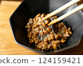 在木桌背景上，用筷子攪拌納豆，在黑色碗中形成黏稠的細絲 124159421