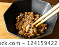 在木桌背景上，用筷子攪拌納豆，在黑色碗中形成黏稠的細絲 124159422