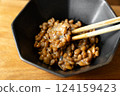 在木桌背景上，用筷子攪拌納豆，在黑色碗中形成黏稠的細絲 124159423