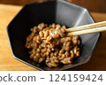 在木桌背景上，用筷子攪拌納豆，在黑色碗中形成黏稠的細絲 124159424