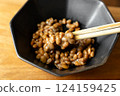 在木桌背景上，用筷子攪拌納豆，在黑色碗中形成黏稠的細絲 124159425