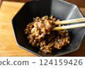 在木桌背景上，用筷子攪拌納豆，在黑色碗中形成黏稠的細絲 124159426