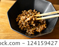 在木桌背景上，用筷子攪拌納豆，在黑色碗中形成黏稠的細絲 124159427