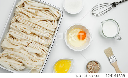 Crinkle Cake baking, filo dough in a baking dish near milk, eggs, butter, butter, sugar Crinkle Cake baking, filo dough in a baking dish near milk, eggs, butter, butter, sugar 124161839