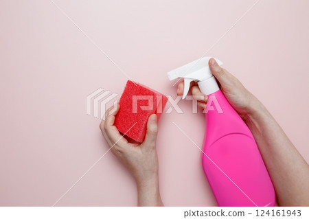 Womans hand in rubber glove holds pink dishwashing sponge and cleaning product. Household cleaning and hygiene concept 124161943