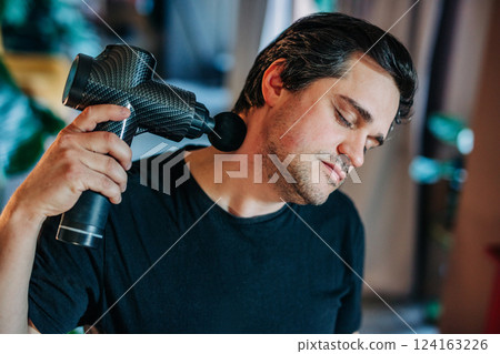 man massages his neck with a handheld electric massager man massages his neck with a handheld electric massager 124163226