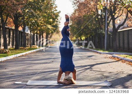 Outdoor yoga woman in headstand, serene morning park setting, peaceful workout, colorful autumn vibes, wellness journey concept 124163968