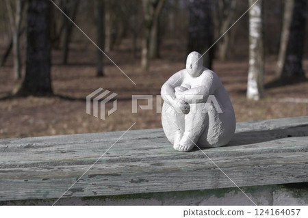 A plaster statue of a full-figured, dreamy woman on a wooden bench in a spring park 124164057