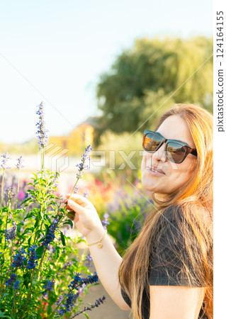 Young woman enjoying scent in blooming spring garden. The concept of youth, love, fashion and lifestyle. 124164155
