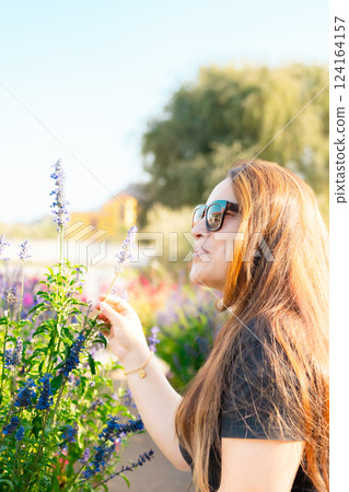 Young woman enjoying scent in blooming spring garden. The concept of youth, love, fashion and lifestyle. 124164157
