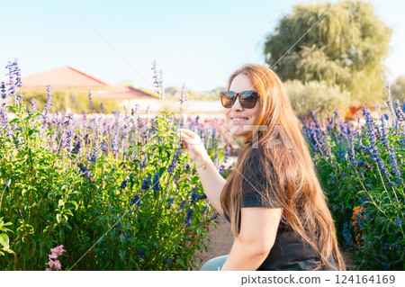 Young woman enjoying scent in blooming spring garden. The concept of youth, love, fashion and lifestyle. 124164169