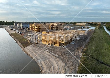 Development of residential housing in American suburbs. Unfinished frames of apartment condos with wooden roof beams under construction. Real estate market in the USA Development of residential housing in American suburbs. Unfinished frames of apartment condos with wooden roof beams under construction. Real estate market in the USA 124164486
