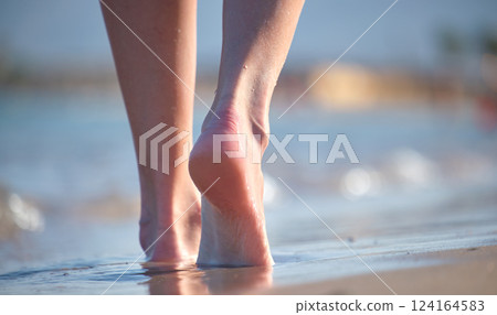 Close up of female feet walking barefoot on white grainy sand of golden beach on blue ocean water background Close up of female feet walking barefoot on white grainy sand of golden beach on blue ocean water background 124164583