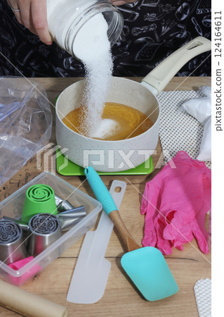 A woman adds sugar to apple juice in a saucepan. She is preparing syrup for homemade marshmallows. Zefir-making tools are nearby on the table. 124164611