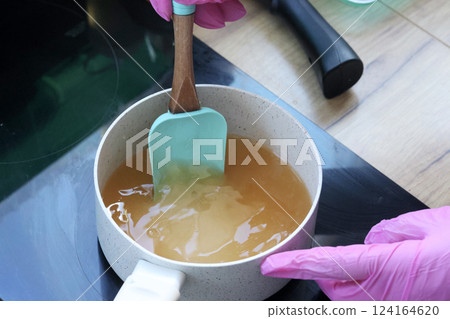 A woman stirs syrup in a saucepan with a spatula. She is preparing syrup for marshmallow mixture. 124164620