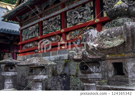 Stone lanterns covered in moss stand in front of elaborately decorated walls Toshogu Shrine in Nikko 124165342