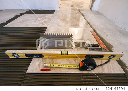 Ceramic tiles and tools for tiler. Floor tiles installation. Home improvement, renovation - ceramic tile floor adhesive, trowel with mortar, level, measuring tape Ceramic tiles and tools for tiler. Floor tiles installation. Home improvement, renovation - ceramic tile floor adhesive, trowel with mortar, level, measuring tape 124165594