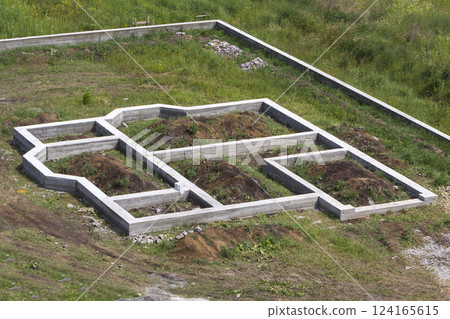 Building site in green field. Trenches dug in ground and filled with cement as foundation for future house and fence around territory. Building, construction, investment and real property concept. Building site in green field. Trenches dug in ground and filled with cement as foundation for future house and fence around territory. Building, construction, investment and real property concept. 124165615