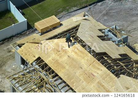Builders working on roof construction of unfinished residential house with wooden frame structure in Florida suburban area. Housing development concept 124165618
