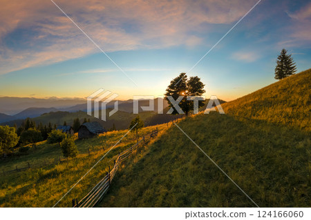 Aerial view of shepherds old wooden hut at colorful sunset in wild mountains. Dark pine forest illuminated with bright setting sun. Beautiful nature landscape Aerial view of shepherds old wooden hut at colorful sunset in wild mountains. Dark pine forest illuminated with bright setting sun. Beautiful nature landscape 124166060