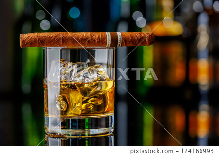 Whiskey on the rocks beside a lit cigar on a bar table Whiskey on the rocks beside a lit cigar on a bar table 124166993
