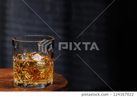 A whiskey glass resting on a wooden table, set against a dark background 124167022