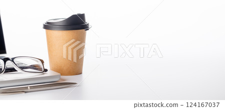 Closeup of an office table featuring a sleek laptop, a coffee cup, and reading glasses on a clean white surface 124167037