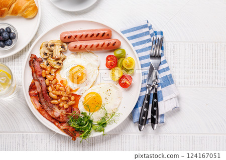 A classic breakfast plate featuring sunny-side-up eggs, crispy bacon, sausages, and fresh tomatoes 124167051
