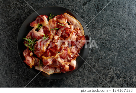 Fried bacon with rosemary on a black stone background. 124167153