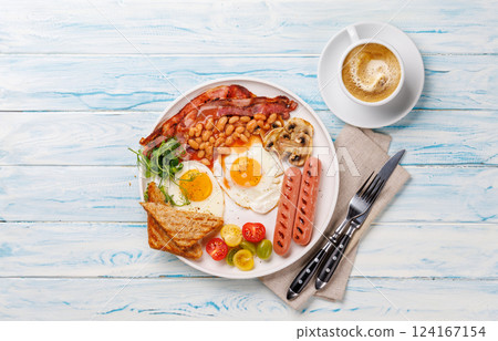 A classic breakfast plate featuring sunny-side-up eggs, crispy bacon, sausages, and fresh tomatoes 124167154