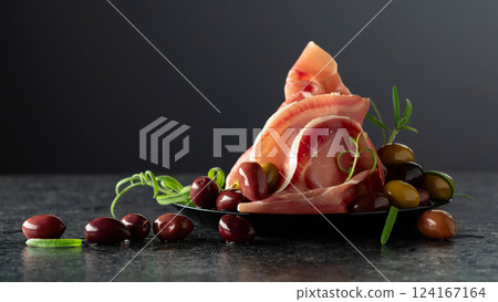Italian prosciutto crudo with olives and rosemary on a black stone table. Italian prosciutto crudo with olives and rosemary on a black stone table. 124167164