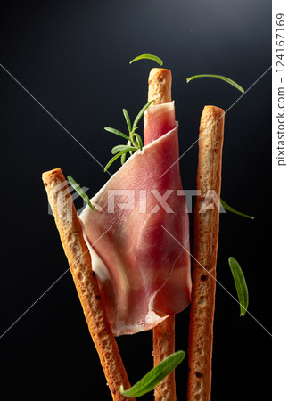 Bread sticks with prosciutto and rosemary on a black background. 124167169