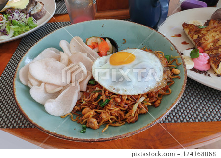 Fried noodles with egg, sausage and meatball toppings served on a wooden table with a garden background Fried noodles with egg, sausage and meatball toppings served on a wooden table with a garden background 124168068