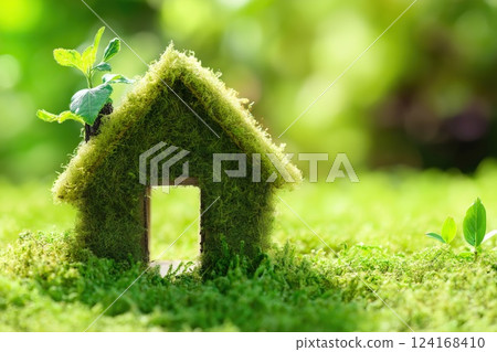 A small house covered in green moss with a sprouting plant growing on the roof, representing eco-living 124168410