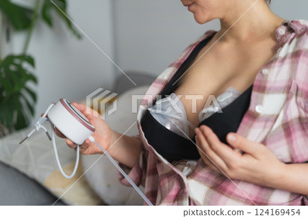 No face woman mom is using electric hands-free breast pump for feeding for her baby. Woman using breast pump while relaxing at home. Comfortable modern Breastfeeding concept. Selective focus. 124169454