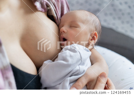 Newborn baby peacefully sleeping after breastfeeding in warm mother embrace at home. No face mother breastfeeding and hugging baby. Lactation infant concept. Baby eating milk before he sleeping. 124169455