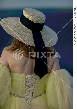 Hat Woman Fashion: Back view of woman with hat, yellow dress likely for a formal event, unknown time. 124169665