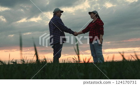 Modern man and woman farmers colleagues shaking hands greeting partnership dramatic sunset sky slowmo. Agricultural worker agronomist agrarian partner handshaking success deal collaboration at field 124170731